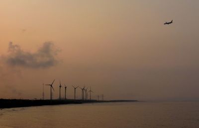 Windmills by sea against sky during sunset