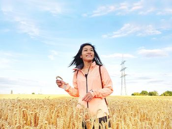 Cheerful woman standing at wheat farm against sky