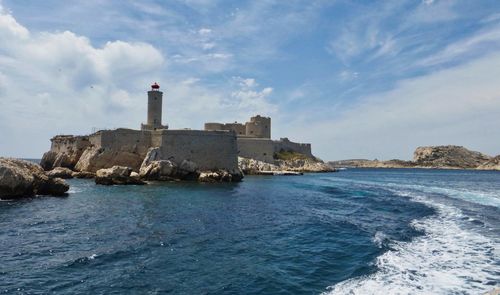 Lighthouse amidst sea and buildings against sky