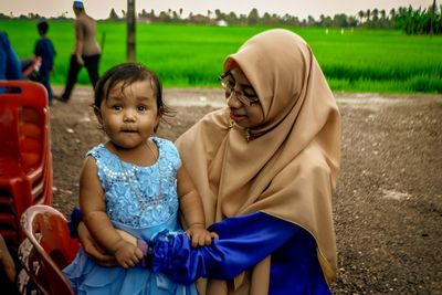 Portrait of cute girl held by mother on field