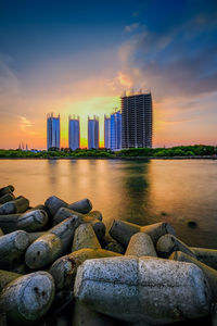 Sea by modern buildings against sky during sunset