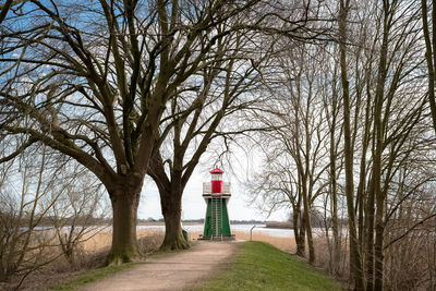 Bare trees by lighthouse against sky