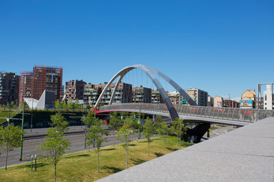 Footbridge over city buildings against clear blue sky