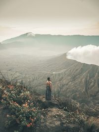 Rear view of man standing on mountain against sky