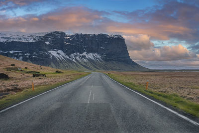 Diminishing road leading towards mountain against cloudy sky during sunset