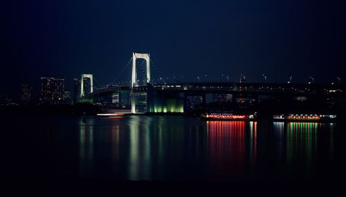 Illuminated buildings by river against sky at night