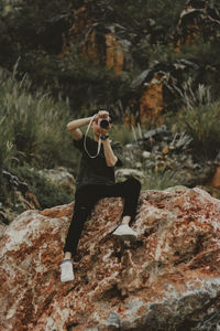 Full length of man photographing while sitting on rock