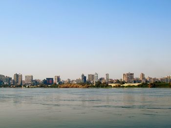 Sea by buildings in city against clear sky