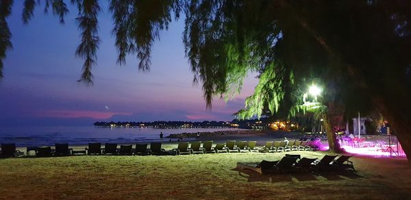 Chairs and tables at beach against sky at night