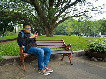 Boy using mobile phone while sitting on bench at park