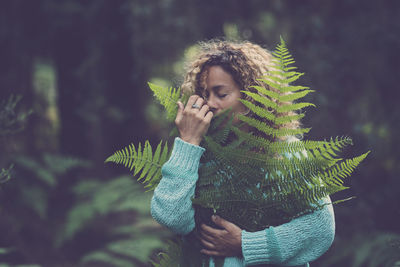 Young woman wearing mask standing against plants during winter