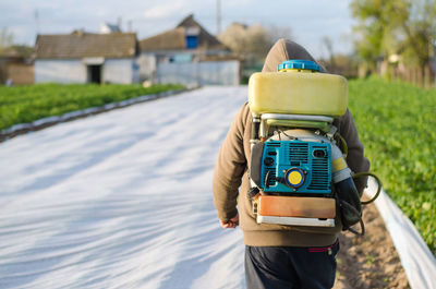 A farmer with a mist sprayer on his back walks through the farm field. protection of cultivated