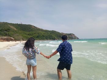 Rear view of couple at beach against sky