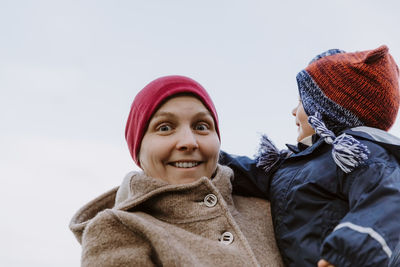 Portrait of mother carrying baby girl against clear sky