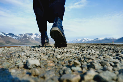 Low section of man walking on rocks against sky