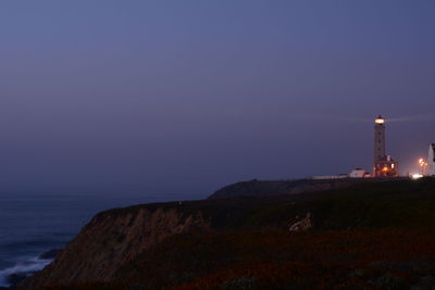 Lighthouse by sea against clear sky at night