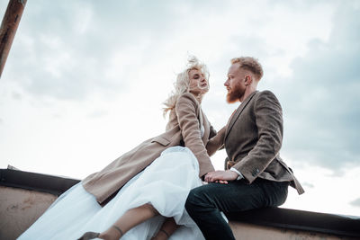 Low angle view of couple sitting against sky