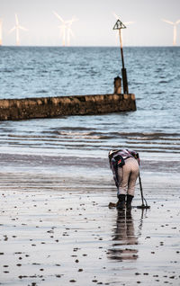 Rear view full length of woman with metal detector at beach