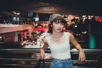 Portrait of young woman standing in footbridge at night