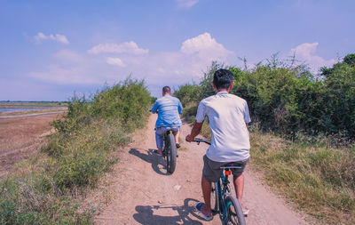 Rear view of men riding bicycle on road against sky