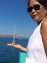 Optical illusion of woman wearing sunglasses holding boat on sea against blue sky