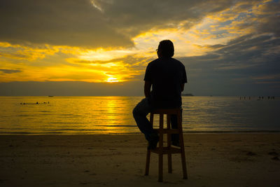 Rear view of silhouette man sitting on beach at sunset
