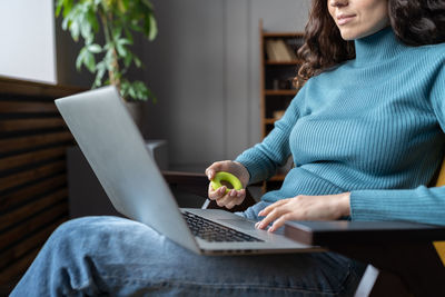 Female employee exercising with hand expander while working on laptop computer in office