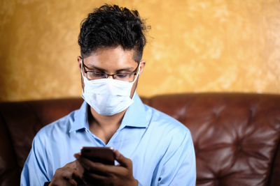 Man wearing flu mask using smart phone sitting on sofa