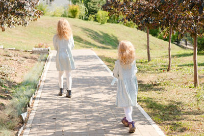 2 little blonde girls with curly hair are walking in a summer park.