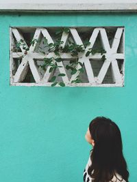 Woman looking at plant growing on turquoise wall