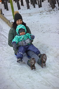 Mother and toddler daughter tobogganing on snow covered field