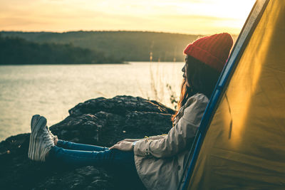 Side view full length of woman relaxing by lake on rock