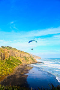 Parasailing over sea by cliff against sky