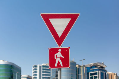 Low angle view of road sign against clear blue sky