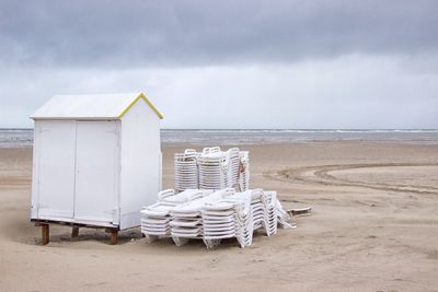 Deck chairs on beach against sky