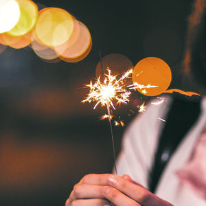 Close-up midsection of woman holding burning sparkler at night