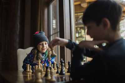 Siblings playing chess by window at home