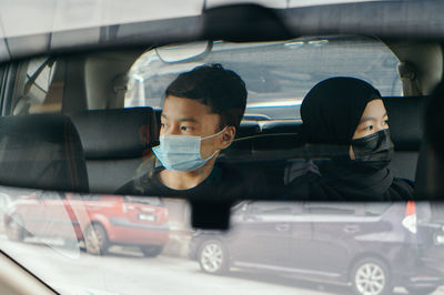 Young woman and boy wearing mask sitting in car