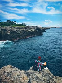 People sitting on rock by sea against sky