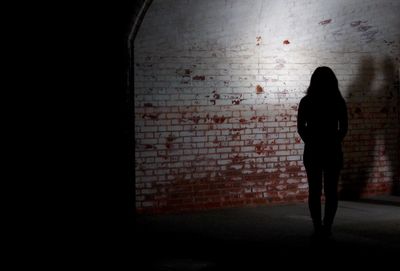 Rear view of silhouette woman standing against brick wall