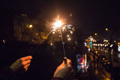 Cropped hands holding illuminated sparklers at night