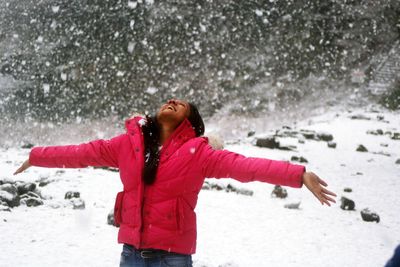 Woman standing with arms outstretched during snowfall