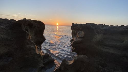 Rock formations on shore against sky during sunset