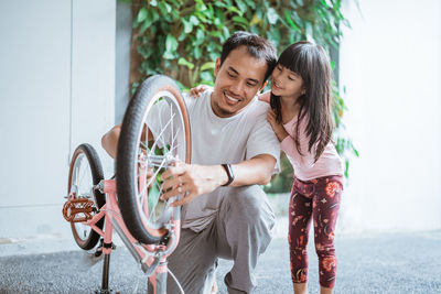 Smiling father repairing bicycle with daughter at home