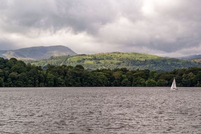 Sailboat sailing in river against mountains and sky