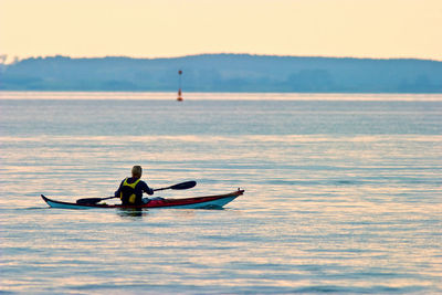 Man rowing boat in sea against sky
