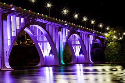 Illuminated purple bridge over river at night