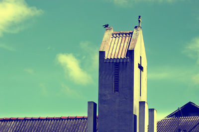 Low angle view of bird perching on roof against sky