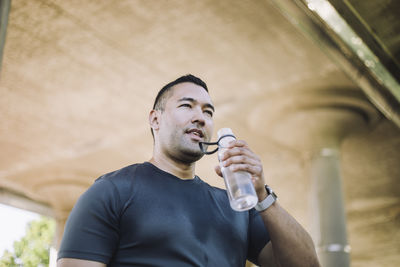 Low angle view of tired man drinking water from bottle during workout