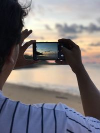 Rear view of man photographing through smart phone at beach during sunset